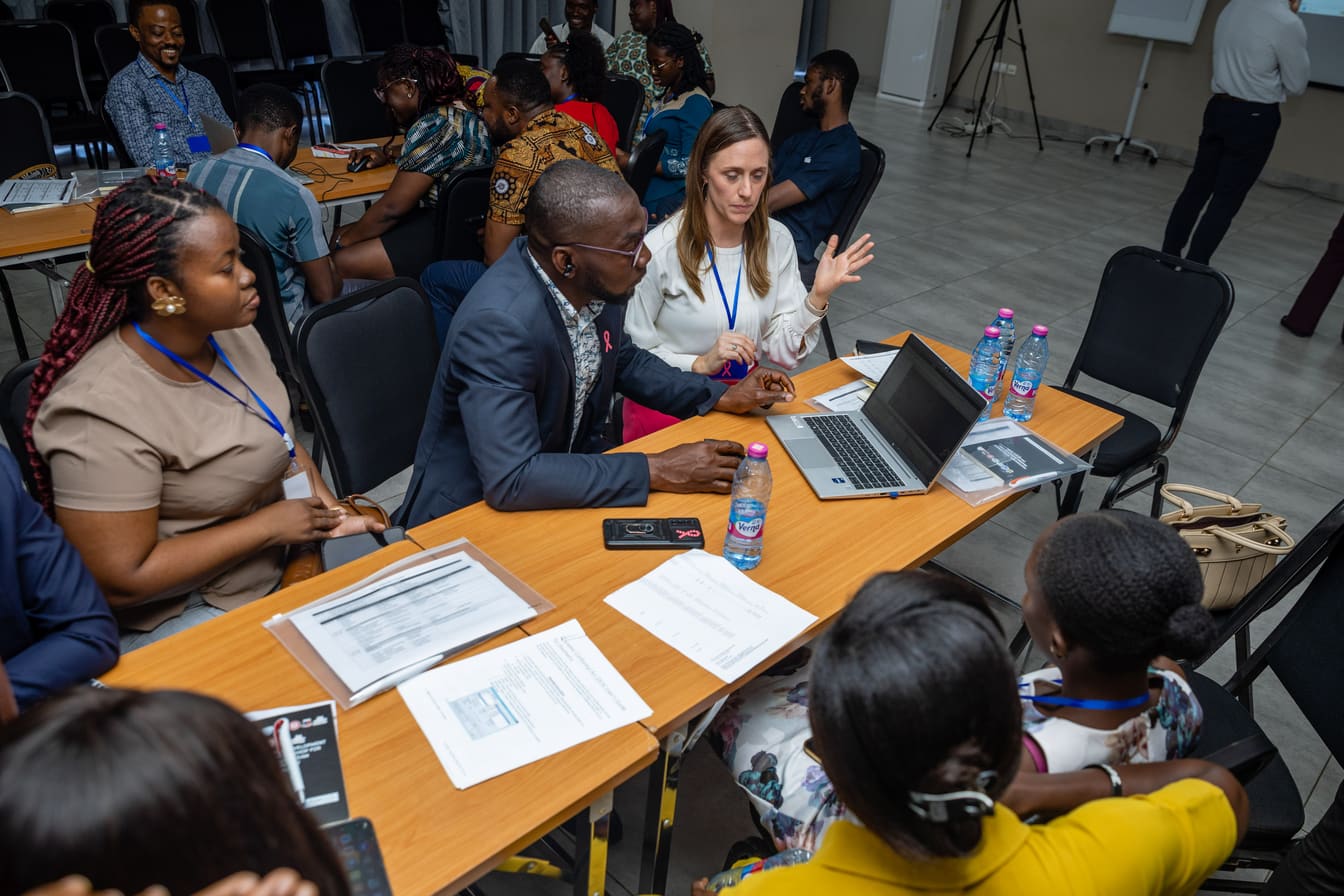 Facilitators and participants in close discussion around a laptop during a COTC Africa workshop session