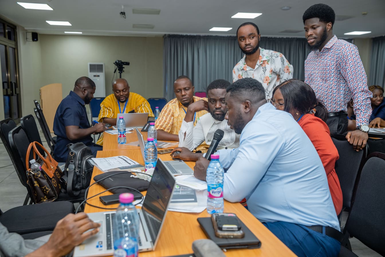 Participants gathered closely around a laptop and microphone during a COTC Africa workshop session